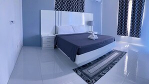 Une chambre à coucher moderne avec un grand lit, une table de chevet, une commode et un tapis à motifs.