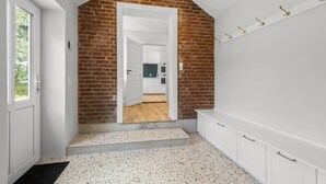 A hallway with a brick wall, a white door, and a kitchen visible through an open door. - Beautiful home in Varde with kitchen (Varde)
