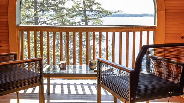 A wooden deck with two chairs and a table, overlooking a body of water and trees.
