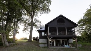 A two-story wooden house with a balcony, surrounded by trees.