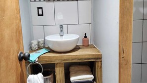 A bathroom with a white sink, a mirror, and a wooden vanity with towels and a basket. - Cabaña Bulnes (Natales)