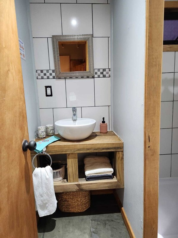 A bathroom with a white sink, a mirror, and a wooden vanity with towels and a basket.