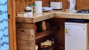 A compact kitchen with wooden cabinetry, a white refrigerator, a coffee machine, and a kettle. - Cabaña Bulnes (Natales)