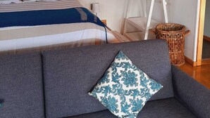 A bedroom with a bed, a sofa, a small table, and a hanging chair. - Cabaña Bulnes (Natales)