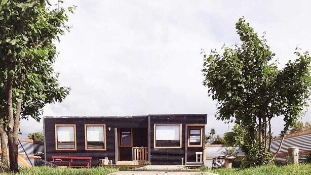 A modern two-story building with large windows and a flat roof, surrounded by trees and a wooden deck. - Cabaña Bulnes (Natales)