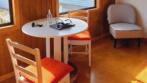 A room with a round table, two chairs, a clock on the wall, and a window with a view of a body of water. - Cabaña Bulnes (Natales)