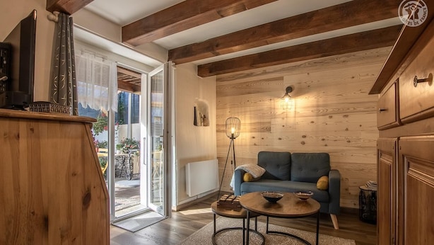 A cozy living room with a blue sofa, wooden beams, a floor lamp, and a view through a glass door. - LA Petite Maison - Bonvillard (BONVILLARD)