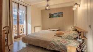 A bedroom with a bed, a wooden bench, a nightstand, a painting, and a balcony with a view. - LA Petite Maison - Bonvillard (BONVILLARD)