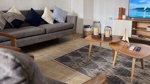 A living room with a grey sofa, patterned cushions, a coffee table with candles, a TV, and a small sailboat model.