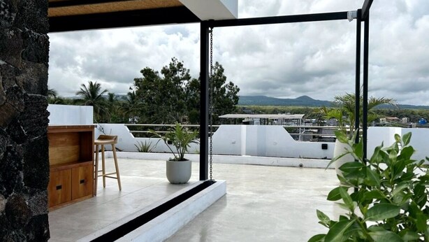A rooftop terrace with a wooden bench, a potted plant, and a view of the cityscape and mountains.