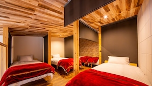 Habitación de hotel con suelo de madera, dos camas con ropa de cama roja y blanca, pared de ladrillo y un diseño moderno en el techo.