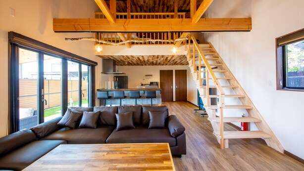 Un espacio habitable moderno con techo y escalera de madera, un sofá grande y una mesa de comedor.