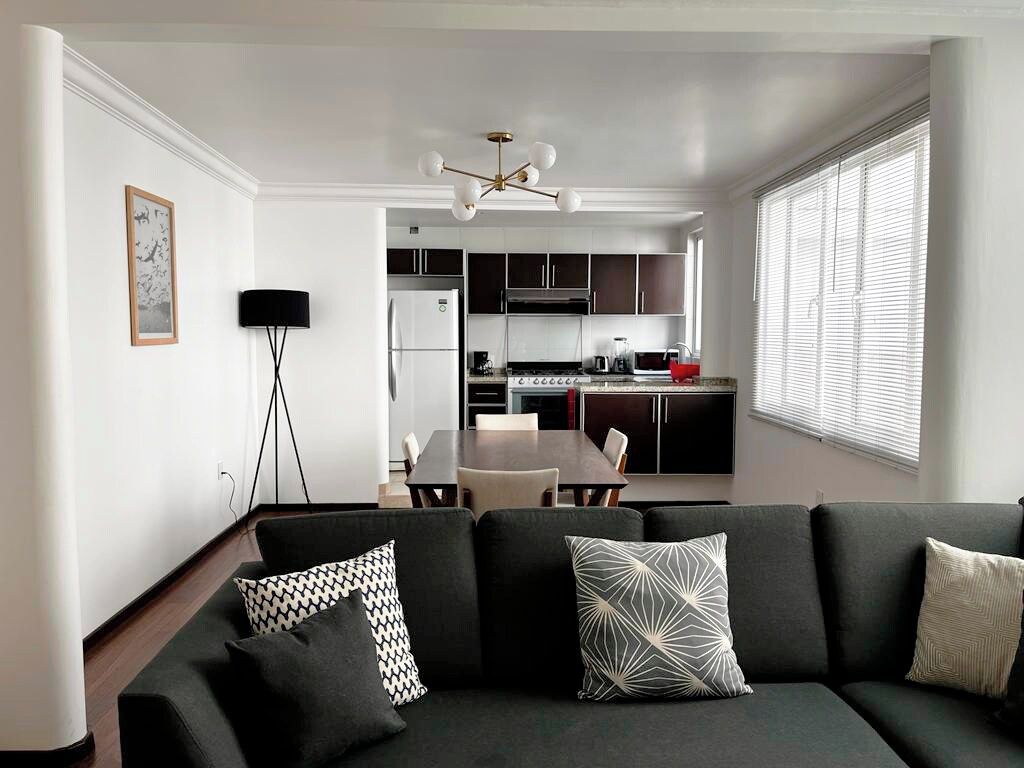 Een moderne woonkamer met een donkere bank, een eettafel en een keuken op de achtergrond.