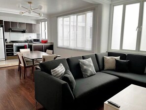 Ein modernes Wohnzimmer mit einer schwarzen Couch, einem Esstisch und einer Küche im Hintergrund.