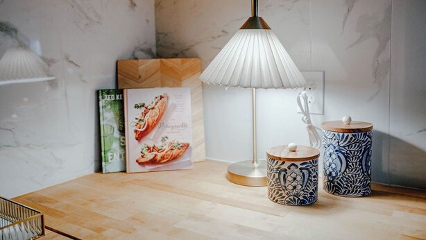 Una cocina moderna con salpicadero de mármol, una lámpara de pie, frascos decorativos y un menú enmarcado sobre la encimera.