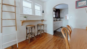 Una cocina con piso de madera, una escalera de madera, dos taburetes y una mesa de comedor con sillas.