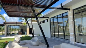 Eine moderne Außenpatio mit einer Pergola, großen Fenstern und zeitgemäßer Sitzgelegenheit.