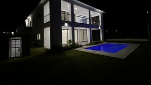 Ein modernes, zweistöckiges Haus mit Swimmingpool, großen Fenstern und gut beleuchteter Fassade.