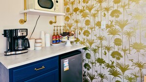 Una cucina con macchina da caffè, forno a microonde e frigorifero. Sopra il bancone, scaffali con oggetti decorativi.