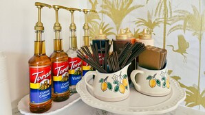 Un ripiano da cucina con bottiglie di sciroppo Torani, una macchina per il caffè e tazze di ceramica decorative.