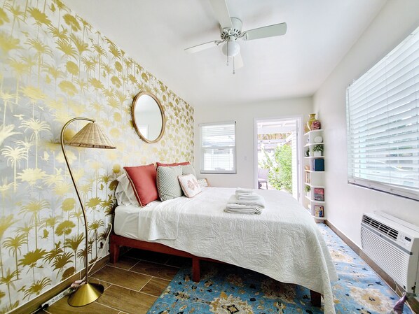 A bedroom with a bed, a ceiling fan, a window with blinds, a radiator, and a patterned rug.