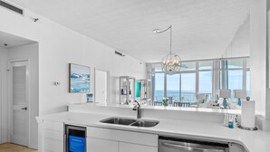 Une cuisine moderne dotée d’un grand îlot central, d’appareils électroménagers en acier inoxydable et offrant une vue sur l’océan.