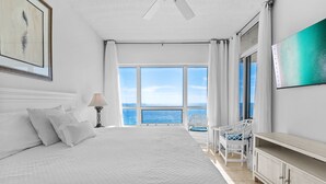 Une chambre avec un grand lit, un bureau, une chaise, une télévision et une vue sur la mer.