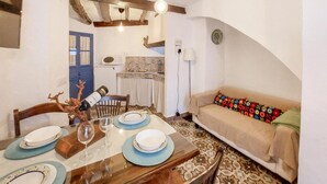 A dining area with a wooden table set for four, a sofa with a colorful cushion, and a kitchen in the background. - 2 bedroom luxurious home in El Gastor (El Gastor)
