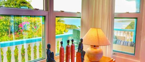 A room with a view of a balcony and a window with a decorative lamp and figurines on a wooden shelf.