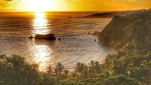 A coastal landscape with a sunset, rocky outcrops, and dense vegetation. - Blue Whale Villa (Calibishie)