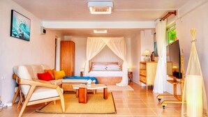A modern hotel room with a bed, a sofa, a coffee table, and a TV. - Blue Whale Villa (Calibishie)