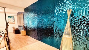 A room with a large blue textured wall, a wooden floor, and a hanging light fixture. - Blue Whale Villa (Calibishie)