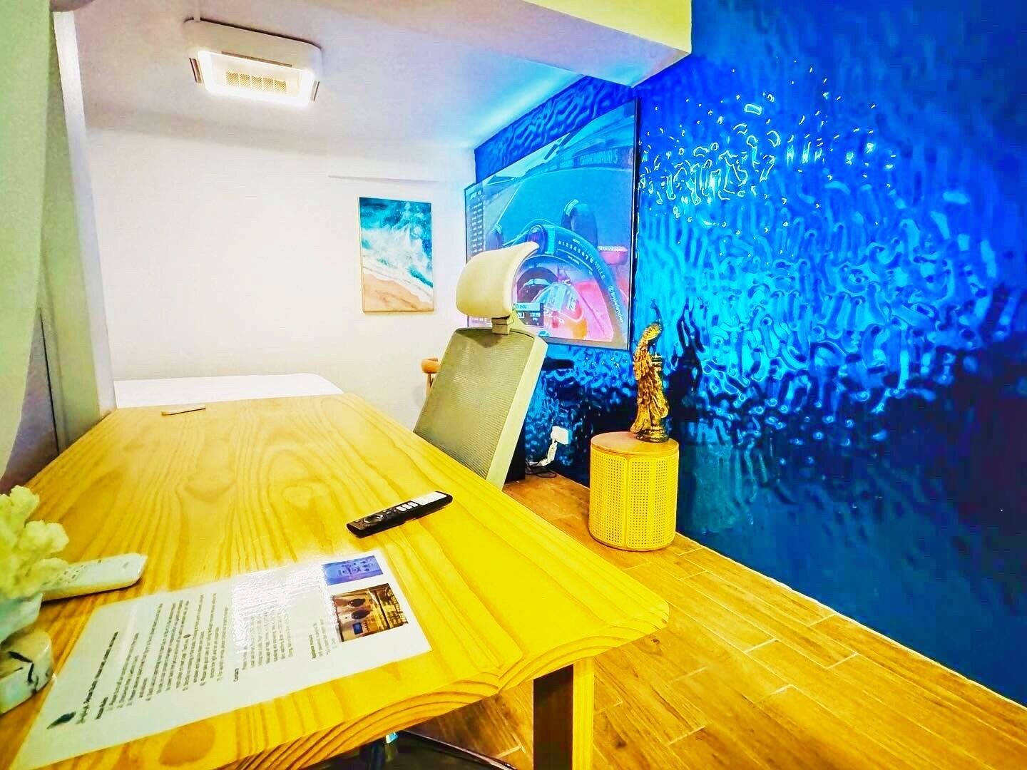 Habitación de hotel con escritorio de madera, una silla, control remoto, lámpara, una estatua decorativa y una pared con diseño abstracto azul.