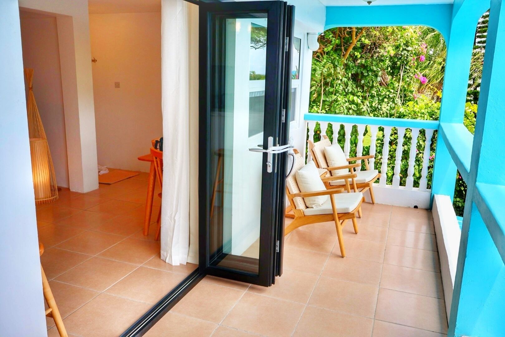 A balcony with a white railing, a glass door, and two wooden chairs.