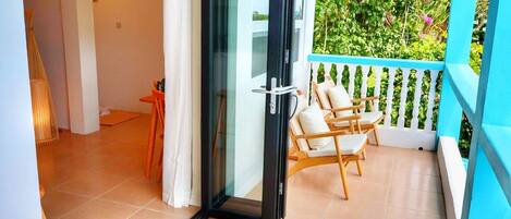 A balcony with a white railing, a glass door, and two wooden chairs.