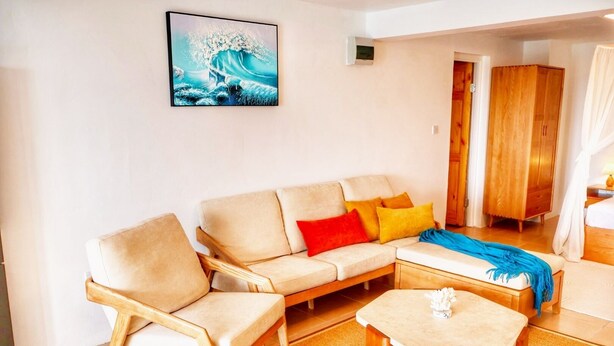 A living room with a beige sofa, a wooden coffee table, and a colorful throw blanket. - Blue Whale Villa (Calibishie)