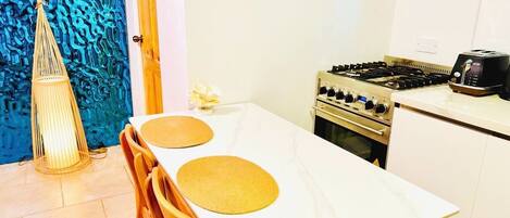 A compact kitchen with a gas stove, a toaster, and a dining table with two placemats.