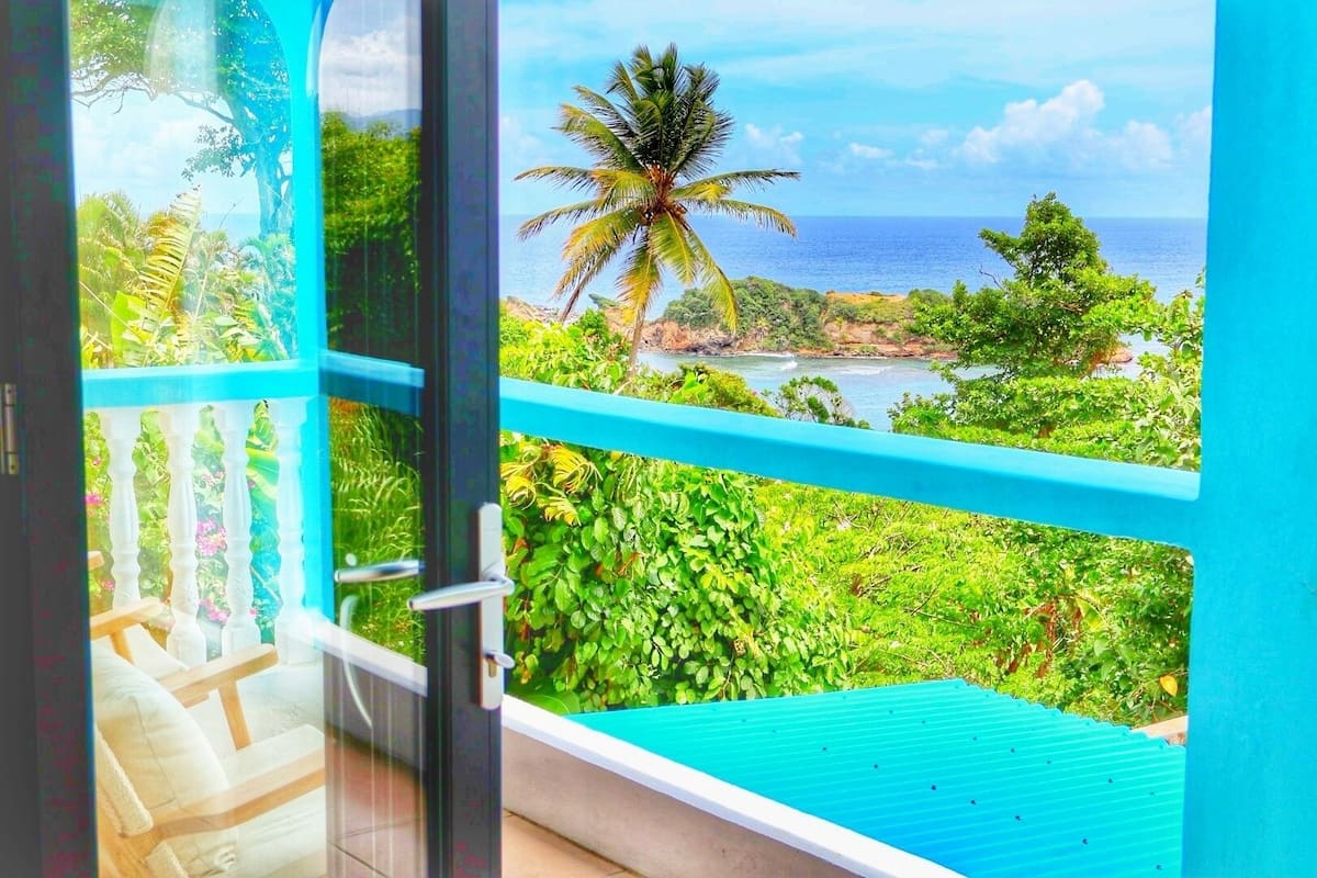 A balcony with a view of a tropical landscape, including a palm tree and the ocean.