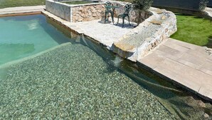 Ein Schwimmbecken mit klarem Wasser, einer Steindeck und zwei Metallstühlen.