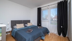 Ein Schlafzimmer mit einem Bett, Nachttischen, einer Lampe und einem Fenster mit Vorhängen.