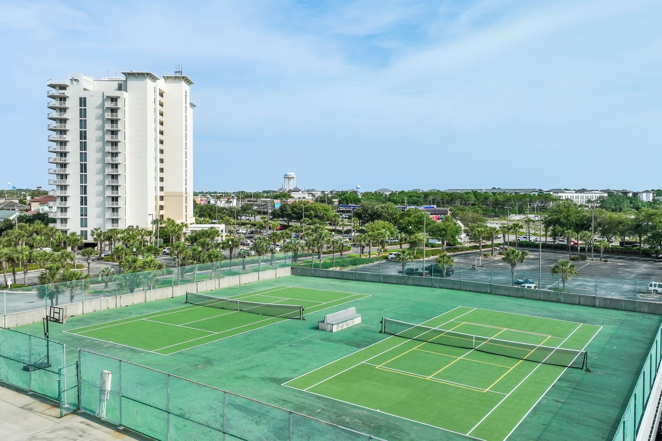 A tennis court with a net, surrounded by a fence, and a tall building in the background.
