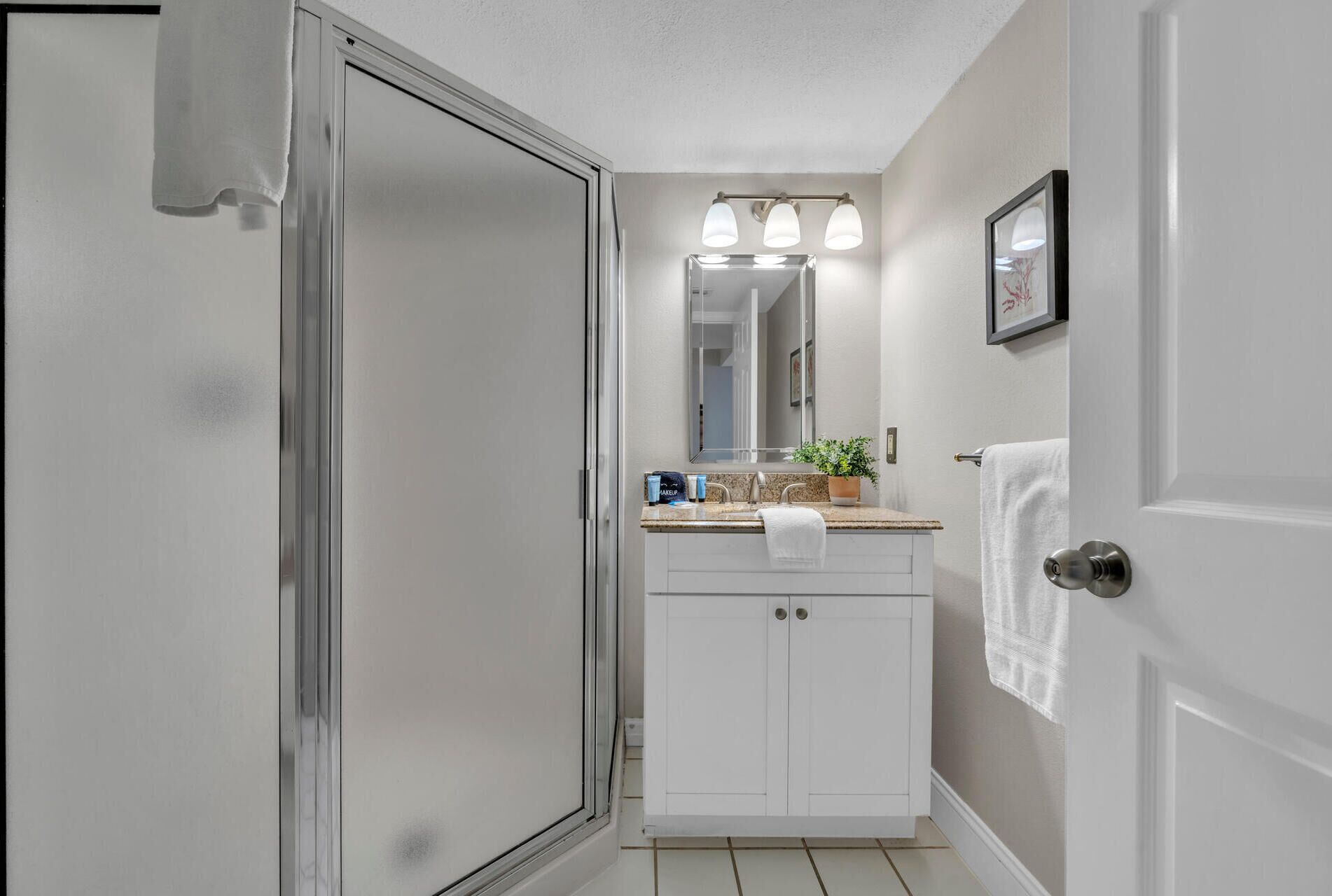 A bathroom with a white vanity, a large mirror, and a towel hanging on the door.