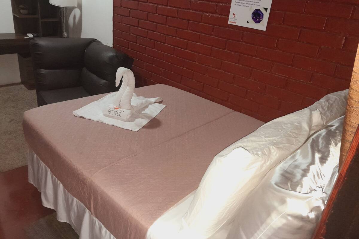 Une chambre d’hôtel avec un lit, un oreiller, une chaise, une lampe et un mur orné d’une plaque.
