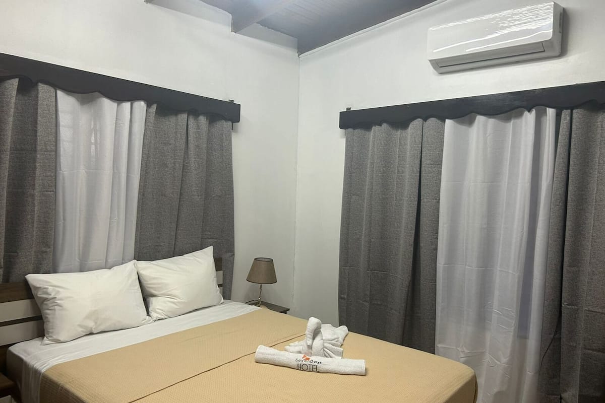 Une chambre d’hôtel avec un lit, deux oreillers, une serviette pliée et un appareil de climatisation fixé au mur.