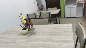 A dining area with a table and chairs, a potted plant, and a small shelf with items. - Seven Days Hotel B&B (San Pedro Sula)