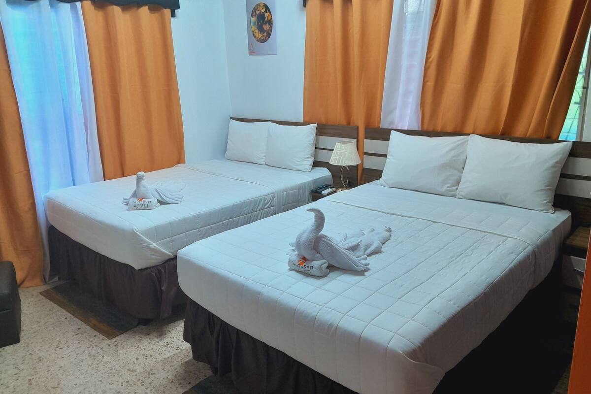 Une chambre d’hôtel avec deux lits, chacun équipé d’une serviette et d’un oreiller. On y trouve une table de chevet avec une lampe et une petite table.