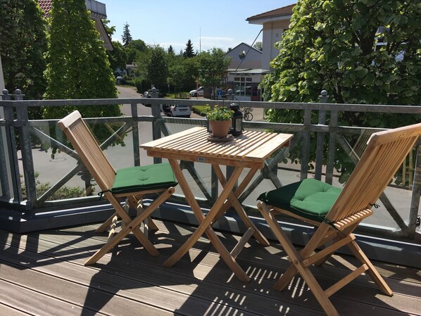 Eine Holzdar Terrasse mit zwei Stühlen und einem Tisch, mit Blick auf eine Straße mit parkenden Autos und Gebäuden.