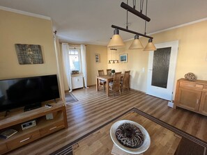 Una sala de estar con televisor, muebles de madera, una mesa de comedor con sillas y un cuenco decorativo.