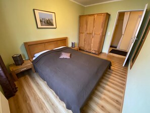 A bedroom with a wooden bed, a nightstand, a wardrobe, and a door leading to another room.