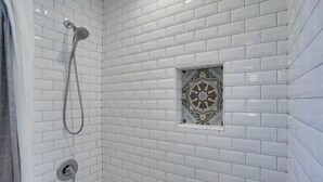 A shower area with white subway tiles, a showerhead, and a decorative tile in the corner. - Bright & Airy Culver City Home w/Garden Oasis. Walkable Location + WFH Ready! (Los Angeles)